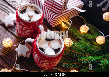 Heiße Schokolade mit Marshmallows und Keksen auf Weihnachtsschmuck Hintergrund. Kissen mit einem Reh, Garland und Tanne gemütliche Atmosphäre schaffen. Stockfoto