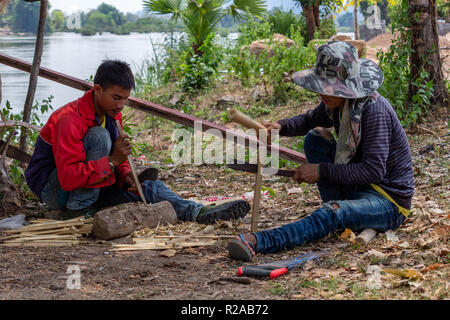 Don Det, Laos - April 24, 2018: Lokale Männer manuelle arbeitet mit Bambus in der Nähe des Mekong River Stockfoto