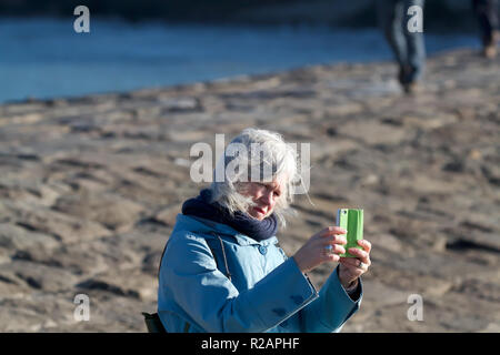 Cornwall, UK. Nov 2018 18. Eine Dame macht ein Foto von der rauen See mit Ihrem Telefon, während auf der Mole in Bude, Cornwall steht. Credit: Keith Larby/Alamy leben Nachrichten Stockfoto