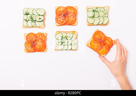 Woman's Hand nehmen Toast mit Tomaten und Chia Samen unter anderen pflanzlichen Sandwiches, Flachbild Layout auf weißem Hintergrund mit kopieren. Stockfoto