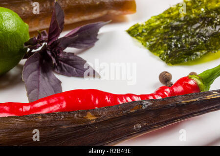 Immer noch leben - geräucherte Hornhecht mit Kalk, Basilikum, grüne Zwiebeln, Chili, Nori Chips, Gewürze, Olivenöl in eine weiße Keramik Teller, auf einem Holztisch Stockfoto