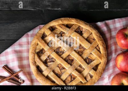 Rustikale Tabelle mit einer ganzen klassischen Apple Pie auf einem rosa Küche Handtuch, von Apple Obst und Zimt umgeben. Oben betrachten. Hausgemachte gebackene Desserts. Stockfoto