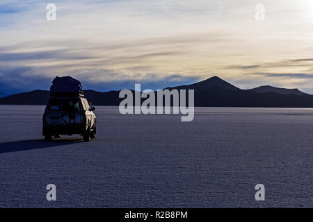 4WD-Fahrzeug parken während des Sonnenuntergangs, in der Mitte des Salar de Uyuni, Bolivien Stockfoto