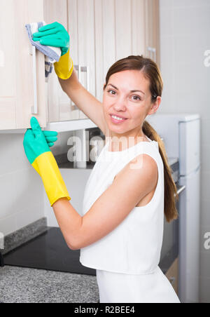 Junge fröhliche Frau das Tragen schützender einheitliche Abwischen von Oberflächen in der Wohnung Stockfoto
