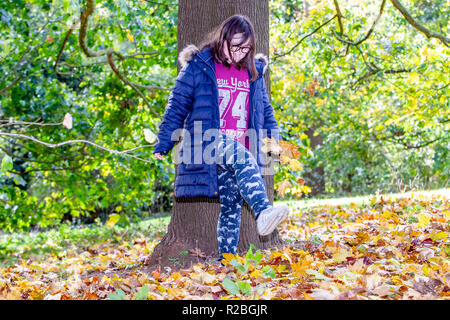 Junges Mädchen mit Down-syndrom im Wald spielen mit dem Laub. Abington Park, Northampton, Großbritannien. Stockfoto