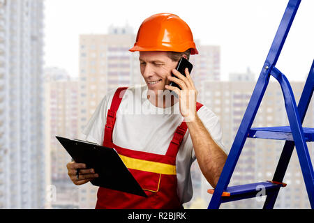 Happy Builder am Telefon sprechen. Lächelnd Techniker sprechen auf dem Smartphone während die Zwischenablage mit Dokumenten. Diskussionen über neue Projekt. Stockfoto