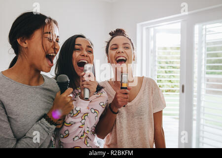 Drei Mädchen singen Holding Mikrofone in Ihrem Zimmer stehen. Glückliche Mädchen Karaoke singen zu einem sleepover. Stockfoto