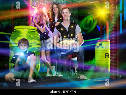 Portrait von Happy Kids und ihre Eltern mit Laserwaffen in farbigen Balken während der Laser tag spiel in dunklen Zimmer Stockfoto