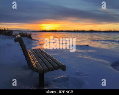 Sitzbank im Winter mit den Sonnenuntergang an der Grenze zu Saint Lawrence River hervorgehoben - gefroren romantische Landschaft Stockfoto