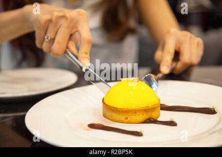 Frau mit Besteck geschnitten frisch gebackene leckere hausgemachte Artisan Pudding Sahne Zitrone Törtchen mit dunkler Schokolade Dekoration. Lebensmittelzutat, Kuchen, Bäckerei, p Stockfoto
