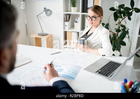 Zuversichtlich Dame mit Becher im Gespräch mit finanzieller Berater im Büro Stockfoto