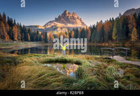 Mann mit erhobenen Waffen auf Antorno See mit Reflexion der Tre Cime di Lavaredo bei Sonnenaufgang im Herbst in den Dolomiten, Italien. Landschaft mit glücklichen Menschen, Gr Stockfoto