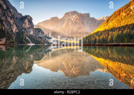 Schöne Pragser See bei Sonnenaufgang im Herbst in den Dolomiten, Italien. Landschaft mit Bergen, gold Sonnenlicht, Wasser mit Reflexion, Bäume mit orange leav Stockfoto