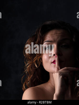 Mädchen, die die Stille, das Modell hat braunes Haar mit Locken und rote Nägel und Lippen auf schwarzen Hintergrund, das Foto hat Platz für Text Stockfoto