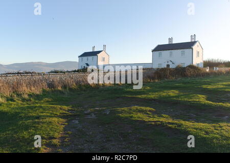 Zwei einsame Hütten an der Küste in der Nähe des Leuchtturms Penmon auf der wunderschönen walisischen Insel Anglesey. Wintersonne beleuchtet die Szene und wirft Schatten. Stockfoto