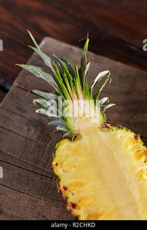 Die Hälfte der Ananas mit saftig grünen Blättern auf einem Holzbrett auf dem Küchentisch. Vitamin Obst. Ansicht von oben Stockfoto