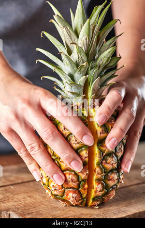 Frische Hälften einer exotischen Ananas halten die Hände der Mädchen auf einer Küche aus Holz. Vitamin Obst Stockfoto