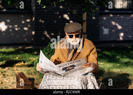 Schöne ältere behinderte Menschen im Rollstuhl lesen Zeitung auf der Straße Stockfoto