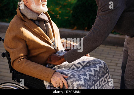 7/8 shot der afrikanischen amerikanischen Mann für ältere behinderte Menschen im Rollstuhl mit Plaid auf der Straße Stockfoto