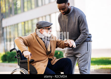 Junge afrikanische amerikanische Mann helfen ältere behinderte Menschen, vom Rollstuhl auf der Strasse zu erhalten Stockfoto