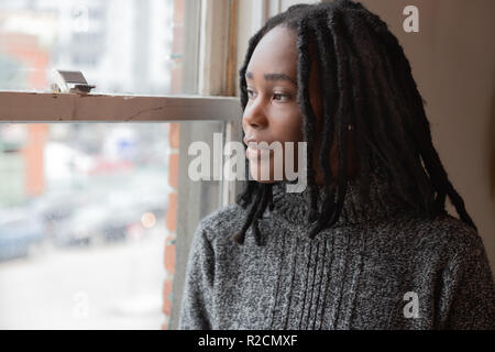 Mädchen mit Dreadlocks blickt Fenster Stockfoto