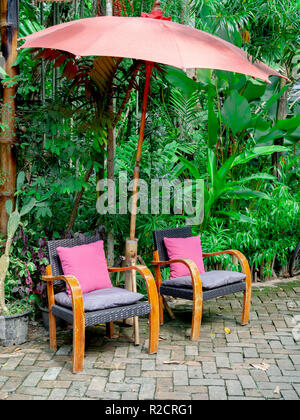 Jahrgang alte Holzstühle mit rosa Kissen und Bambus Sonnenschirm im Garten vertikale Stil. Stockfoto