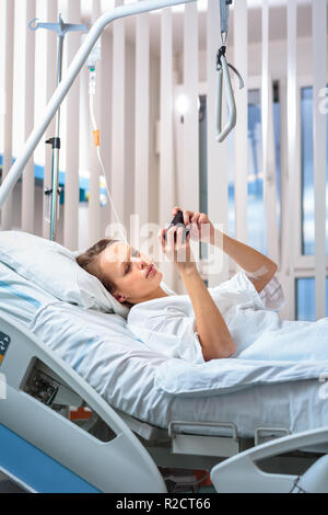 Hübsche, junge, weibliche Patienten in einem modernen Krankenzimmer. Immer besser schnell nach einer Operation - nachdenklich noch positiv, vorausdenken, Pläne (sha Stockfoto