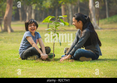 Lächelnd Bruder und Schwester das Einpflanzen einer kleinen Pflanze im Garten und saß neben ihm. Stockfoto