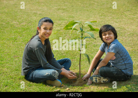 Lächelnden Jungen und Mädchen das Einpflanzen einer kleinen Pflanze im Garten sitzen auf dem Boden. Stockfoto