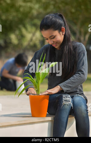 Junge Mädchen das Einpflanzen einer kleinen Pflanze in einem Topf im Garten sitzen mit einem Jungen im Hintergrund sitzen. Stockfoto