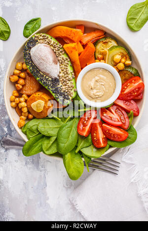 Vegan buddha Schüssel mit gebackenem Gemüse, Kichererbsen, Avocado und tahini Dressing auf einem weißen Hintergrund, Ansicht von oben, kopieren. Stockfoto