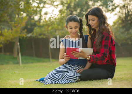 Glückliche Frau und Tochter in einem Garten sitzen an einem Buch suchen. Stockfoto