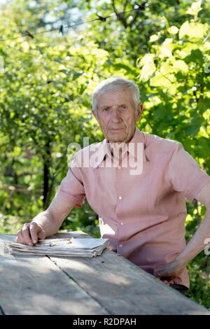Portrait von älteren Mann an einem Tisch sitzen im Garten Stockfoto