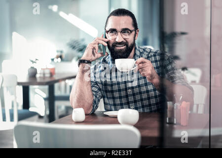 Dark-eyed Mann, Quadrat shirt Holding weiße Tasse Kaffee Stockfoto