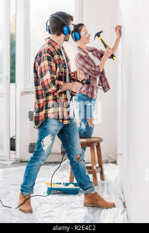 Seitenansicht des jungen Mann mit Bohrmaschine und lächelnde Frau hämmern Nagel in neue Wohnung Stockfoto