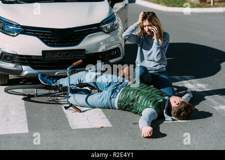 Junge Frau Notrufe und verletzten Radfahrer liegen auf der Straße nach Autounfall Stockfoto