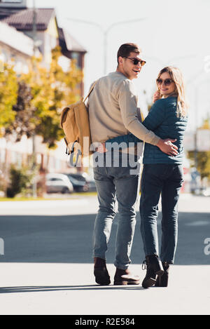 Rückansicht des Paar umarmen und mit Blick auf die Kamera beim Gehen auf der Straße in neue Stadt Stockfoto