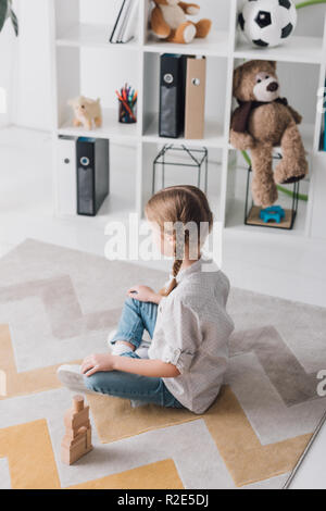 Hohe Betrachtungswinkel von depressiven Kind sitzt auf dem Boden mit Holzklötzen und Wegsehen Stockfoto