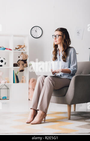 Kinderpsychologen sitzt im Sessel mit Laptop und Wegsehen Stockfoto