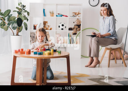 Kleine Kinder spielen mit Bausteinen während Psychologen sitzen auf Hintergrund verschwommen Stockfoto