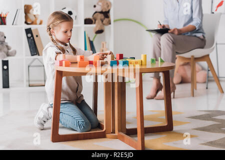 Kleine Kinder spielen mit Bausteinen während Psychologen sitzen auf Hintergrund verschwommen konzentriert Stockfoto