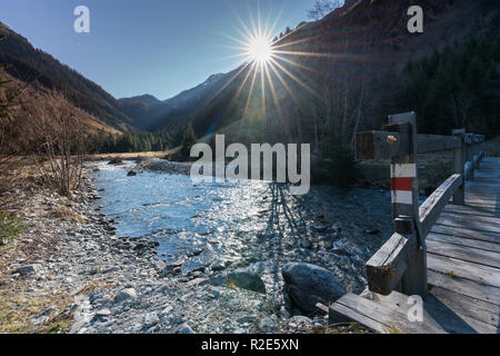 Schönen Bergbach und Peak Landschaft mit Sonne und eine hölzerne Brücke mit einem Wanderweg Zeichen im Vordergrund. Stockfoto