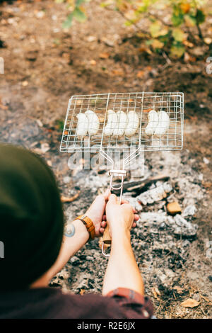 Die Hände des Menschen rösten Reihe mit Würstchen vom Grill Gitter über das Feuer im Herbst Stockfoto