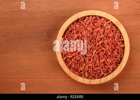 Ein Foto von einem langkornreis Roter Reis, Schuß von oben in eine hölzerne Schüssel auf einem dunklen rustikalen Hintergrund mit Kopie Raum Stockfoto