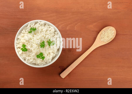 Ein Foto von einer Schale gekocht weiß Langkornreis und ein Löffel von der gleichen Reis ungekocht, geschossen von oben auf einen dunklen Holzmöbeln im Landhausstil Hintergrund mit einem Pla Stockfoto