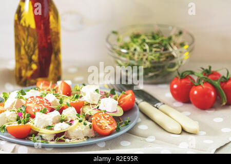 Gesund lecker lecker Salat mit Tomaten, Radieschen, Käse, Sprossen und Sesam in der Platte auf hellem Holztisch, flacher Tiefe des Feldes. Stockfoto