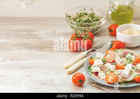 Gesund lecker lecker Salat mit Tomaten, Radieschen, Käse, Sprossen und Sesam in der Platte auf hellem Holztisch, flacher Tiefe des Feldes. Stockfoto