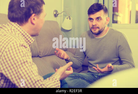 Fröhlicher mensch Sprechen und Lachen mit Freund, während auf dem Sofa zu Hause sitzen Stockfoto