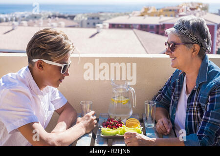 Gerne Freizeitaktivitäten Aktivität auf der Terrasse das Frühstück auf der Dachterrasse mit einem Lächeln und Glück für Großmutter und Teenager Familie kaukasischen Völker. Blick auf das Meer und Gebäude, Coule zusammen Stockfoto