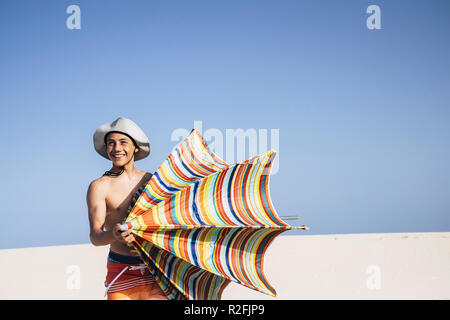 Schöne fröhliche Schöner junge Teenager kaukasischen Völker während der Sommerferien spielen mit einem farbigen Dach Sonne mit weißen Sandstrand und blauer Himmel im Hintergrund. viel Spaß im Urlaub Konzept Stockfoto